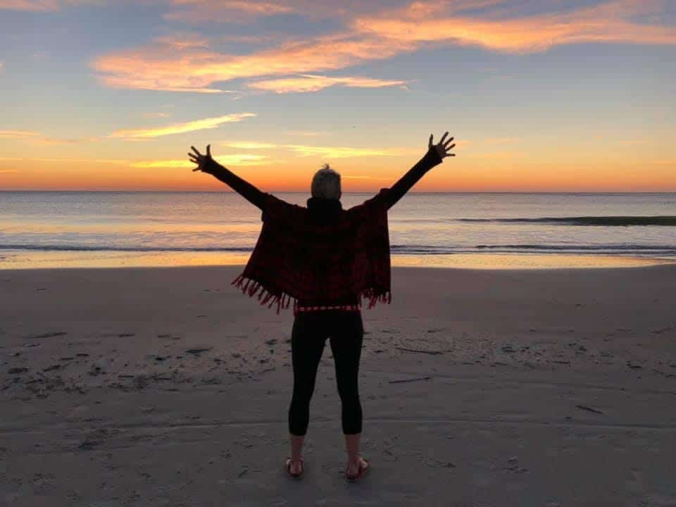 Woman standing on a beach with her arms spread at sunrise